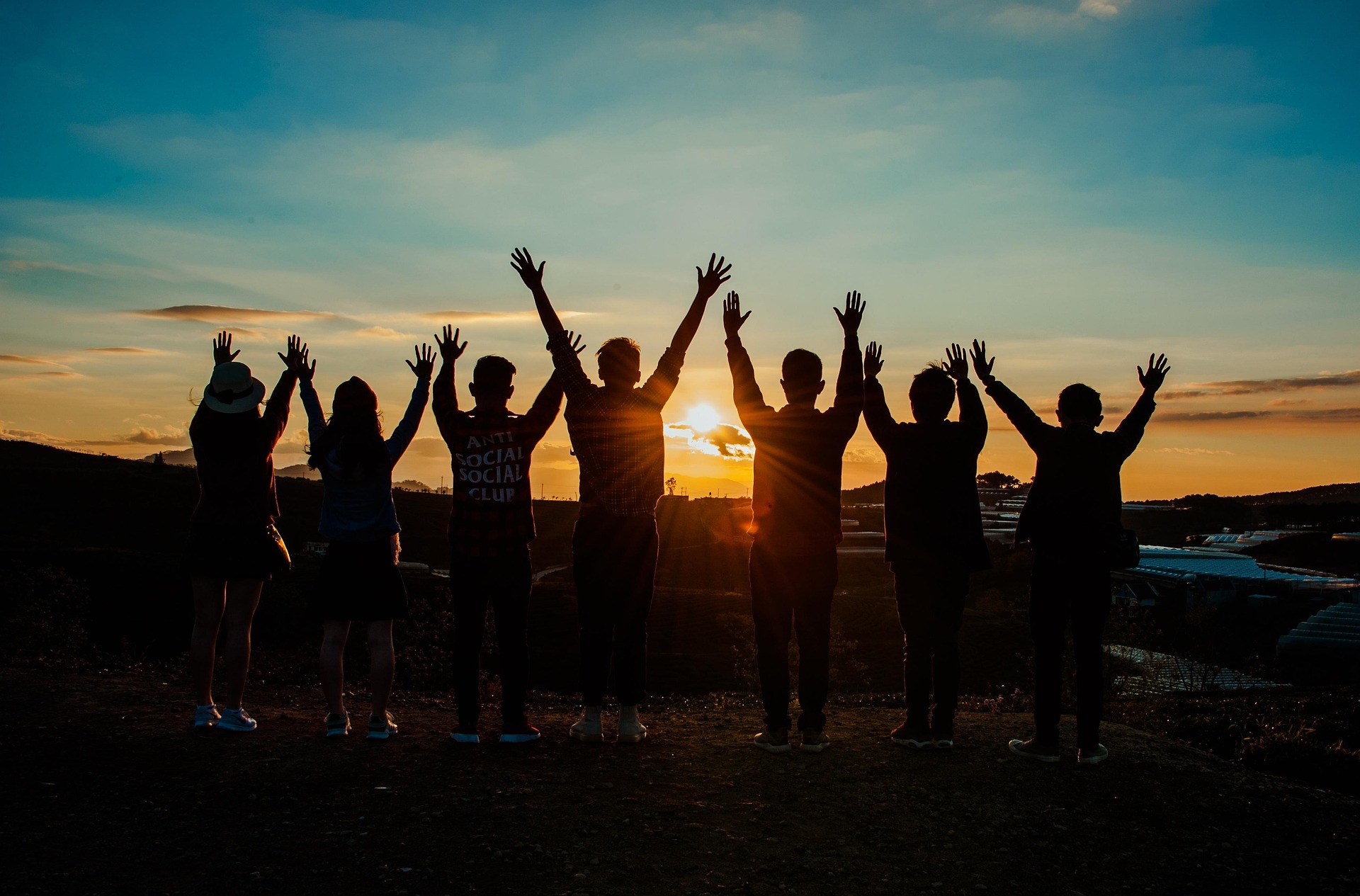 Silhouette of young people with raised hands at sunset